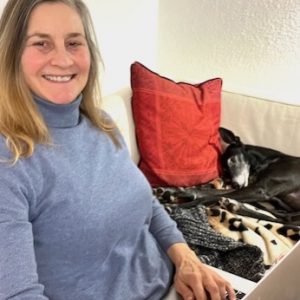 Frau auf Couch mit Laptop auf dem Schoß; Hund liegt daneben und schläft